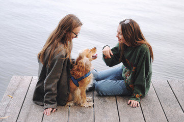 Two girls and english cocker spaniel dog lying on wooden bridge.Portrait of dog outside (outdoors). Sunny day.