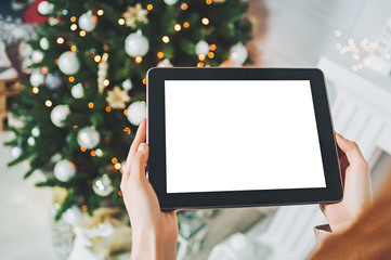 Mock up tablet in the hands of a girl on the background, New Year Christmas tree with holiday decoration.