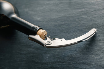Stainless  wine corkscrew in a cork of wine bottle neck on a black slate background