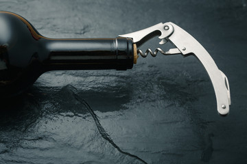 Stainless  wine corkscrew in a cork of wine bottle neck on a black slate background