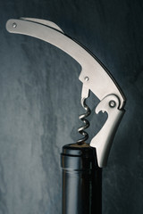 Stainless  wine corkscrew in a cork of wine bottle neck on a black slate background