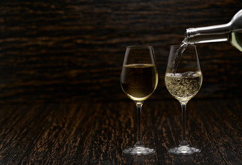 Pouring white wine into the glasses against wooden background