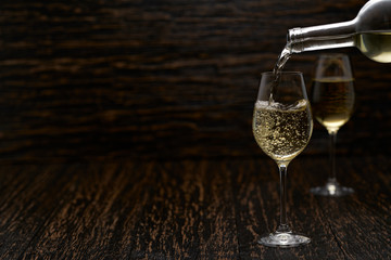 Pouring white wine into the glasses against wooden background