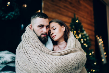 Couple hugging rolled in rug with Christmas tree on background