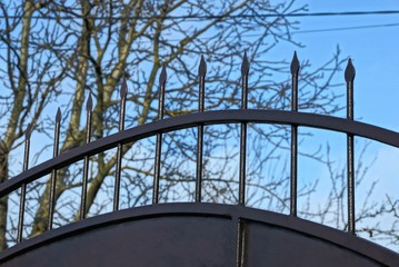 part of a black iron fence with sharp rods against the blue sky and gray branches