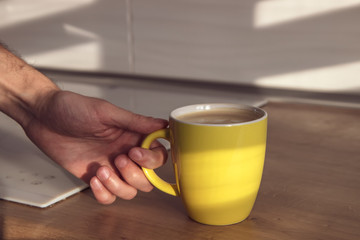 Close-up coffee with milk in hand.Hand of man hold cup of coffee on wood table