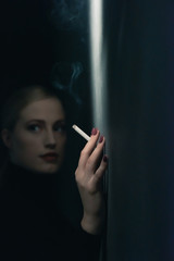 Obraz premium Retro 1940s woman with cigarette in black turtleneck sweater leaning against wall.