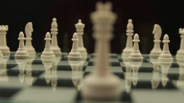 change of focus from a white king to white chess pieces on a chessboard on a black background
