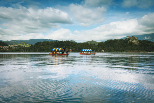 Beautiful landscape of lake Bled (Blejsko jezero) in Slovenia with distant view of tourists taking a ride in traditional local boats called Pletna - Powered by Adobe