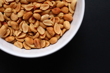 A white bowl with peanuts seen from above with a dark background