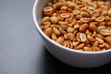 Peanuts in a white bowl on a dark background, seen diagonally from above