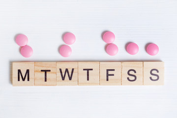The concept of taking medication by day is the process of treatment. Pink tablets next to wooden frames with letters.