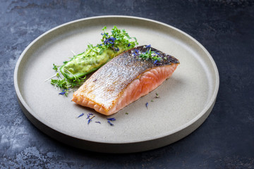 Minimalistic design salmon fish filet glazed with avocado and wasabi creme in a sliced cucumber as...