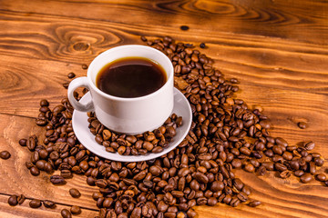 Cup of hot coffee and scattered coffee beans on wooden table