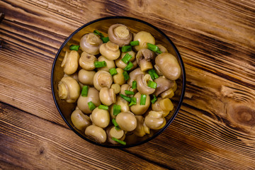 Glass bowl with canned mushrooms and green onion on wooden table. Top view