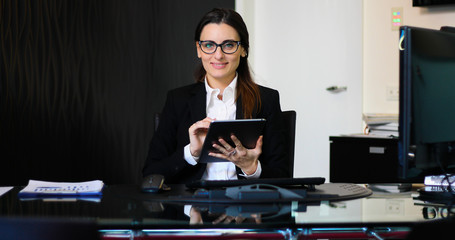 Young thoughtful secretary using a digital tablet at her desk - obrazy, fototapety, plakaty