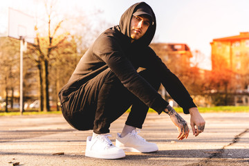 portrait of young rapper posing in the middle of an outdoor basketball court - obrazy, fototapety, plakaty