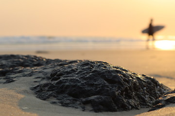 Sunrise, surfer silhouette background, rocks sand foreground