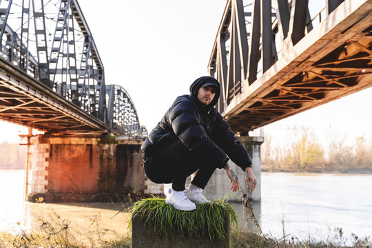 portrait of young rapper posing under a metal bridge