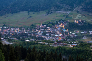 Fototapeta na wymiar Evening view on Mestia with its beautiful illuminated Svan Towers and high mountains. Svaneti, Georgia.