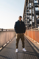 portrait of young rapper posing under a metal bridge