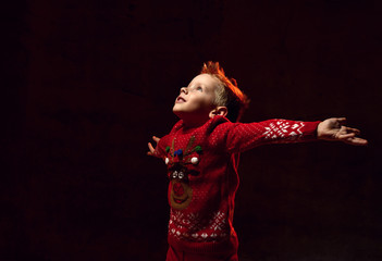 happy little boy in red pullover catching snowflakes in his hands.