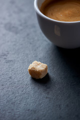 Brown sugar cube and cup of coffee on dark stone background. Close up.