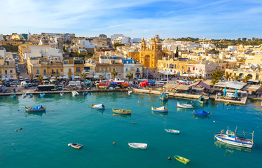 Fototapeta na wymiar Landscape aerial view of fishing village Marsaxlokk. Traditional maltese boats on the sea, main church, coastline, blue sly. Malta