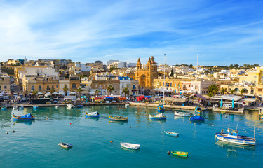 Landscape view of fishing village Marsaxlokk. Traditional maltese boats on the sea, main church, coastline, blue sly. Malta country