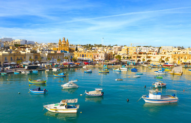 Fototapeta na wymiar Landscape view of fishing village Marsaxlokk. Traditional maltese boats on the sea, main church, coastline, blue sly. Malta island