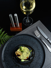 Exquisite fish dish, carpache with caviar and guacamole on a black slate plate. Restaurant sevresing with a glass of white wine