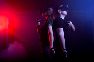 couple in modern glasses of virtual reality play a shooter against a dark neon background, a team of gamers in a game with weapons