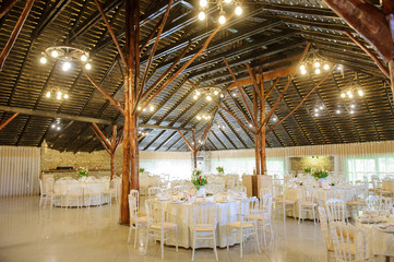 close up photo of the interior of a wedding restaurant: arranged round white tables and wooden pillars