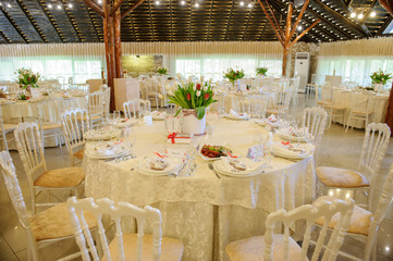 close up photo of a banquet room at a christening party: arranged white round tables with vases with tulips and plates with dishes on it