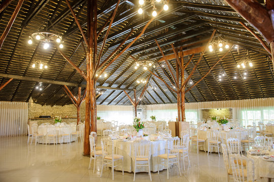 close up photo of the interior of a wedding restaurant: arranged round white tables and wooden pillars
