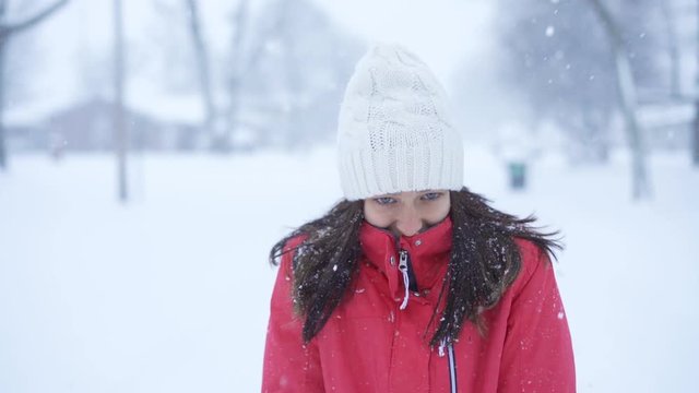 Slow motion of Young woman walking out in the snow during the day while snow is falling around her. She is walking in urban neighborhood.