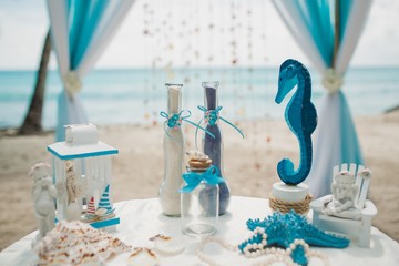 White and blue wedding decorations on a white table on a beach with the sea on the background