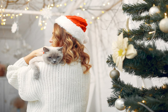 Elegant girl in a white sweater. Woman sitting by the christmas tree. Lady with little kitty