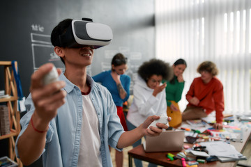 The evolution of VR Technologies. Young asian man in casual clothes wearing wearing virtual reality headset and smiling while his colleagues discussing new project behind him. High Tech