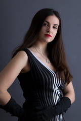 Fototapeta premium Medium vertical portrait of beautiful young brunette in graphic sleeveless black and white top and long evening gloves 