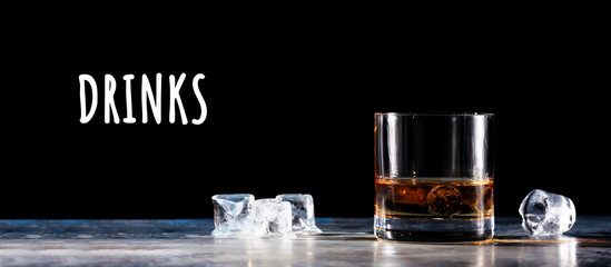 Glass of whiskey on the rocks with some ice on the table. Concept of hard liquor. Horizontal, wide...