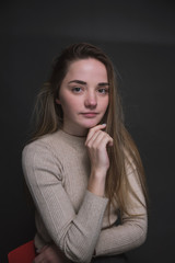 Portrait of a beautiful, sweet, young girl on a gray background in a beige sweater