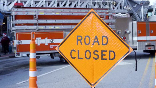 Slow motion of orange sign that reads road closed with fire truck in background because of accident on roadway