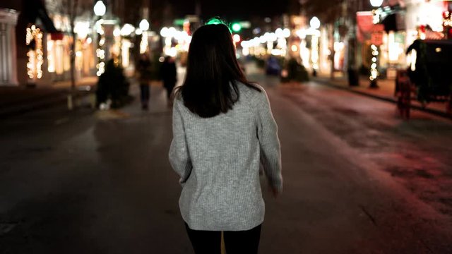 Night time shot of woman walking downtown in middle of street exploring and traveling at night.