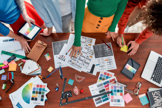 Creating a Brand Book. Top view of design team working on a new project in the creative office. Group of web designers discussing sketches, choosing colors from palettes lying on the desk