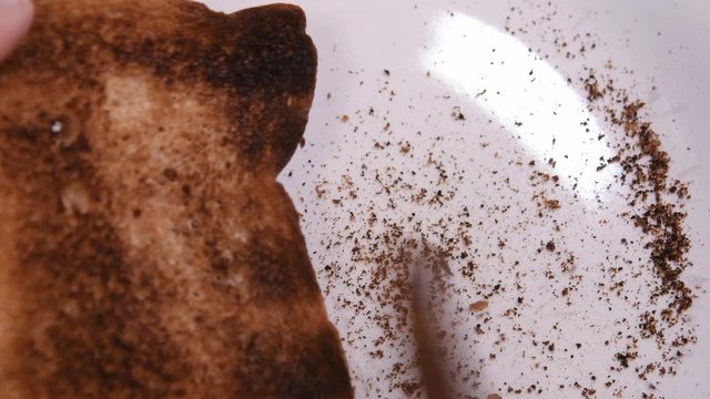 Video scraping burnt toast. Selective focus. Brown bread. Scrape burnt parts of toast with knife. 4K food video.