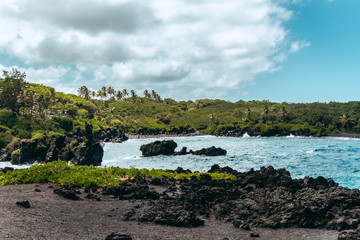coastline of lava and black sand beach blowhole maui road to hana green jungle palmtrees and blue...