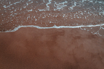 Fototapeta premium black sand beach at sundown with cloud reflections on wet sand waves clear water