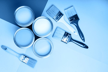 Four open cans of paint with brushes on blue background. Main color of the year 2020 in interior