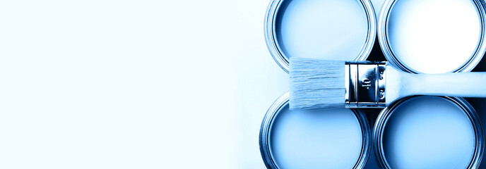 Brush with wooden handle on open cans on blue pastel background. Blue color. Renovation concept....